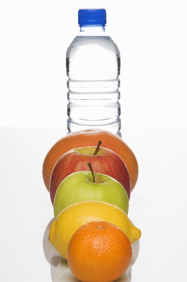 A row of fresh fruit in front of a bottle of water