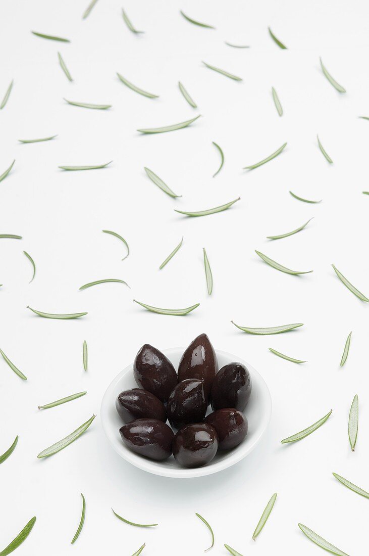 Kalamata-Oliven im Schälchen und verstreute Rosmarinblätter