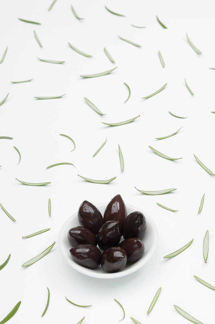 Kalamata olives in a bowl and scattered rosemary leaves