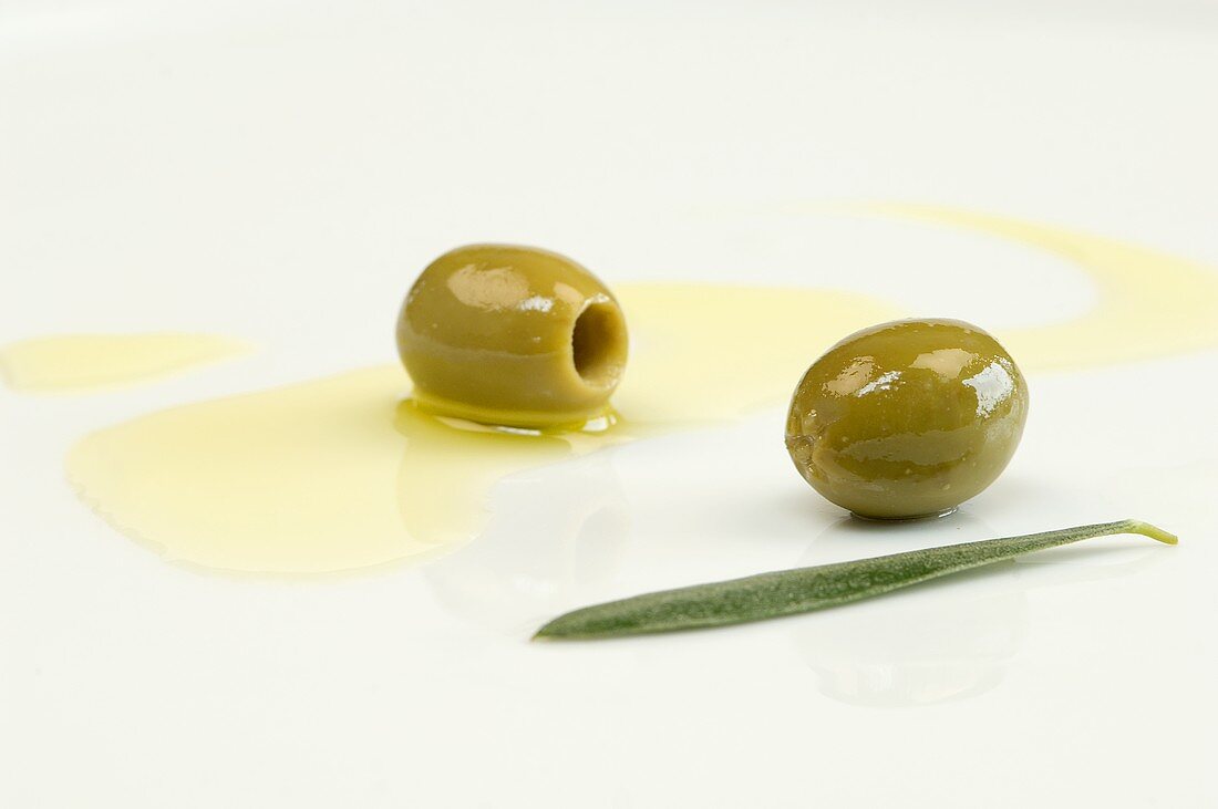 Olivenöl, grüne Oliven und Olivenblatt auf Teller