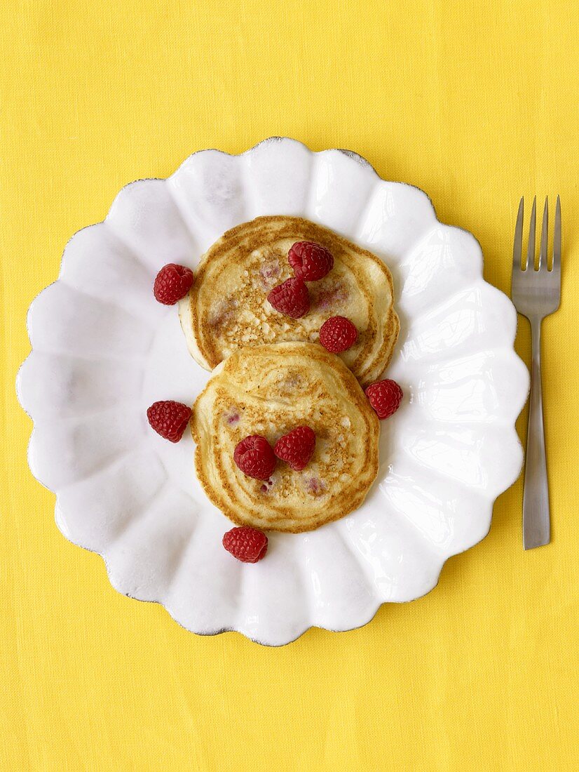 Two Pancakes with Fresh Raspberries on a White Plate; Yellow Background