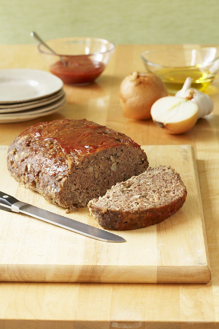 Partially Sliced Meatloaf on Cutting Board; Plates and Ingredients