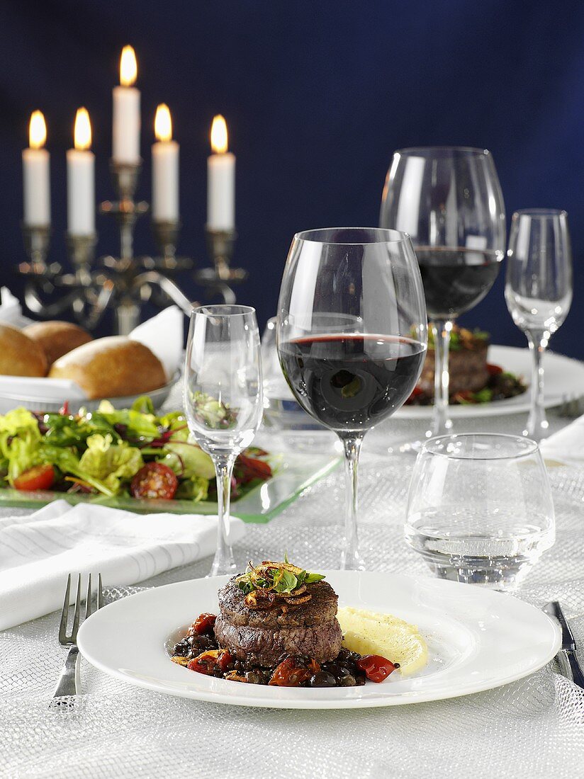 Beef medallions with vegetables, salad and red wine on a laid table
