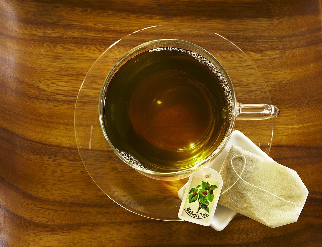 Mulberry Tea (Maulbeertee) in Glastasse von oben, Teebeutel auf Untertasse