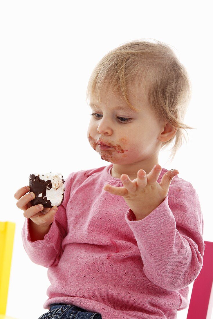 A small child eating a chocolate marshmallow