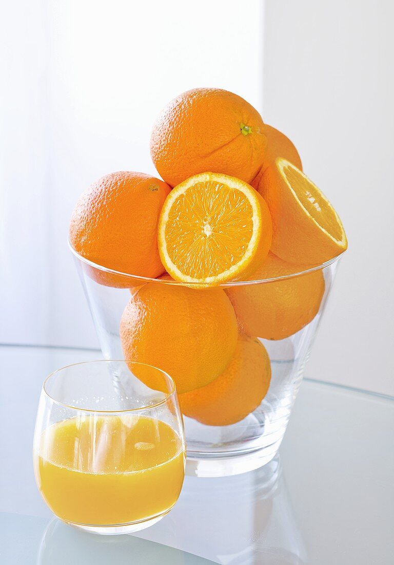 A glass of orange juice and fresh oranges