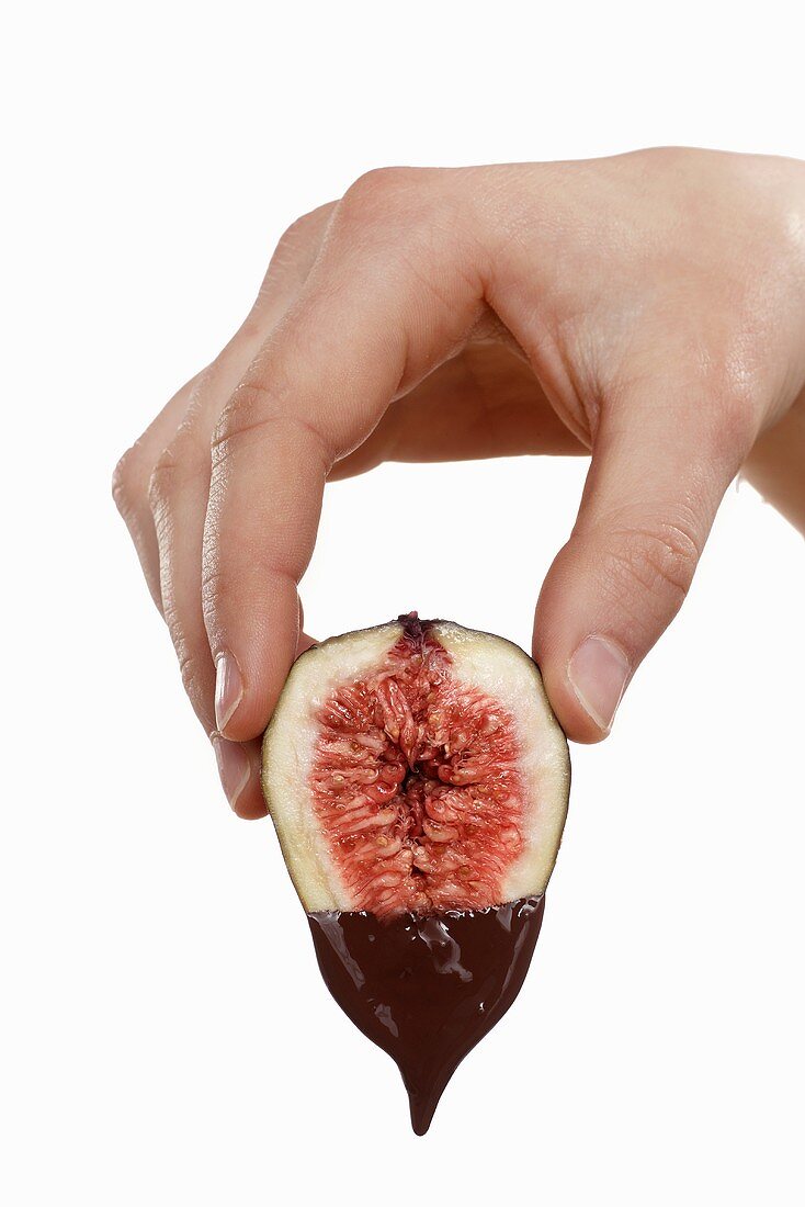 Hand holding a fig dripping with melted chocolate
