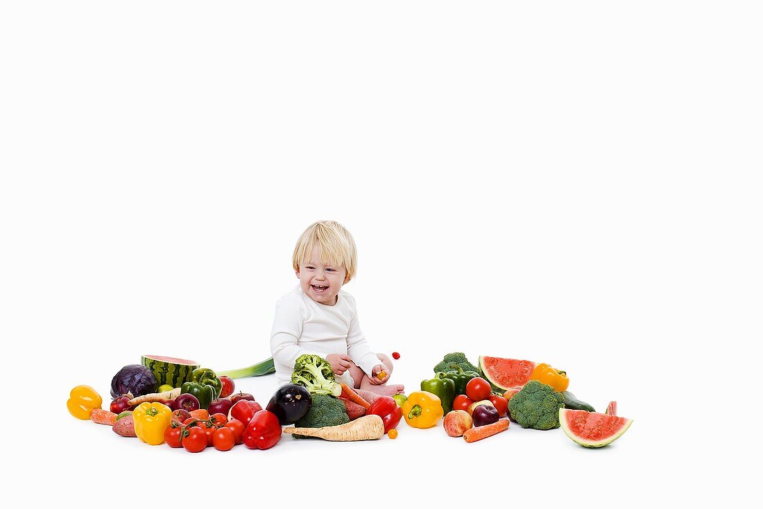 Little child sitting in a the middle of different kinds of colorful vegetables