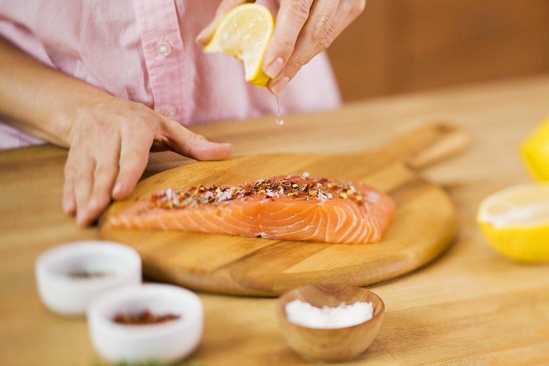 Woman Squeezing a Lemon Wedge over Salmon