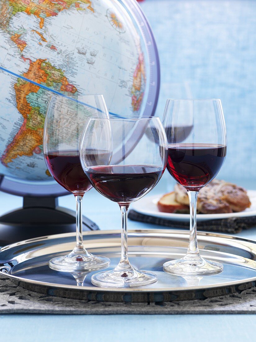 Drei Gläser Rotwein auf einem silbernen Tablett vor einem Globus