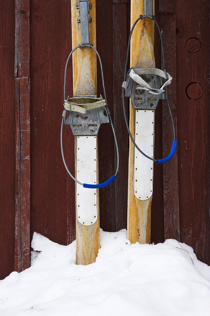 Alte Holzskier stecken im Schnee vor Holzwand