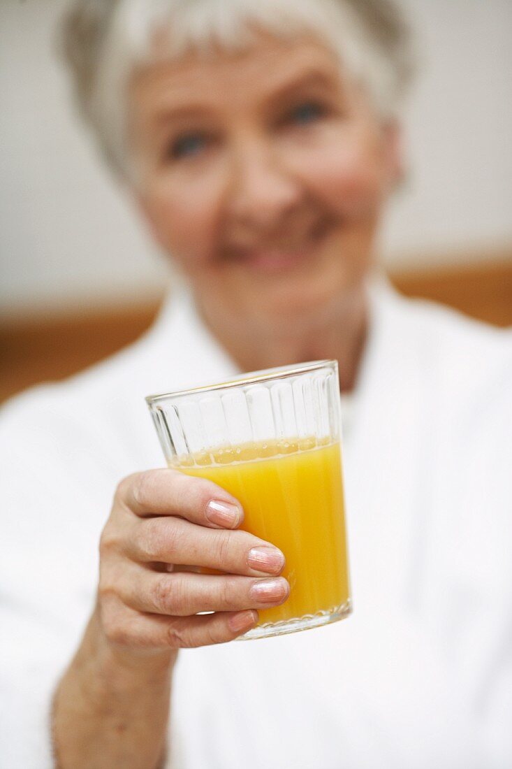 An old woman holding a glass of orange juice