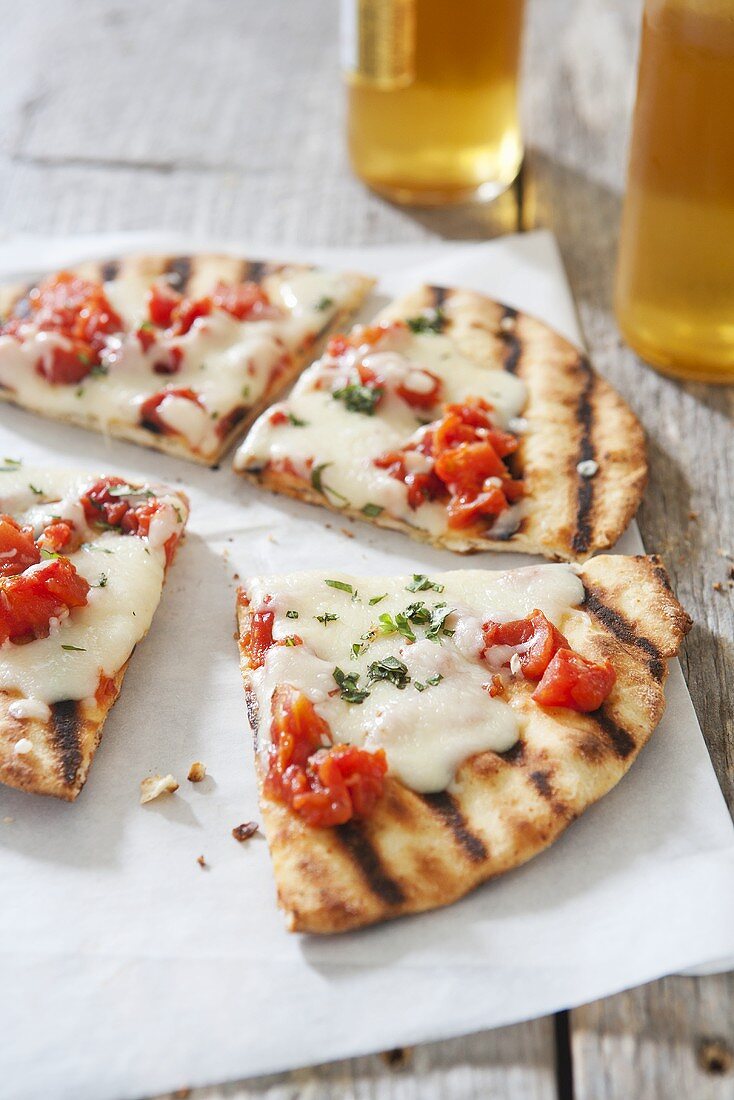 Gegrillte Mozzarella-Tomaten- Pizza auf Tisch, Bierflaschen