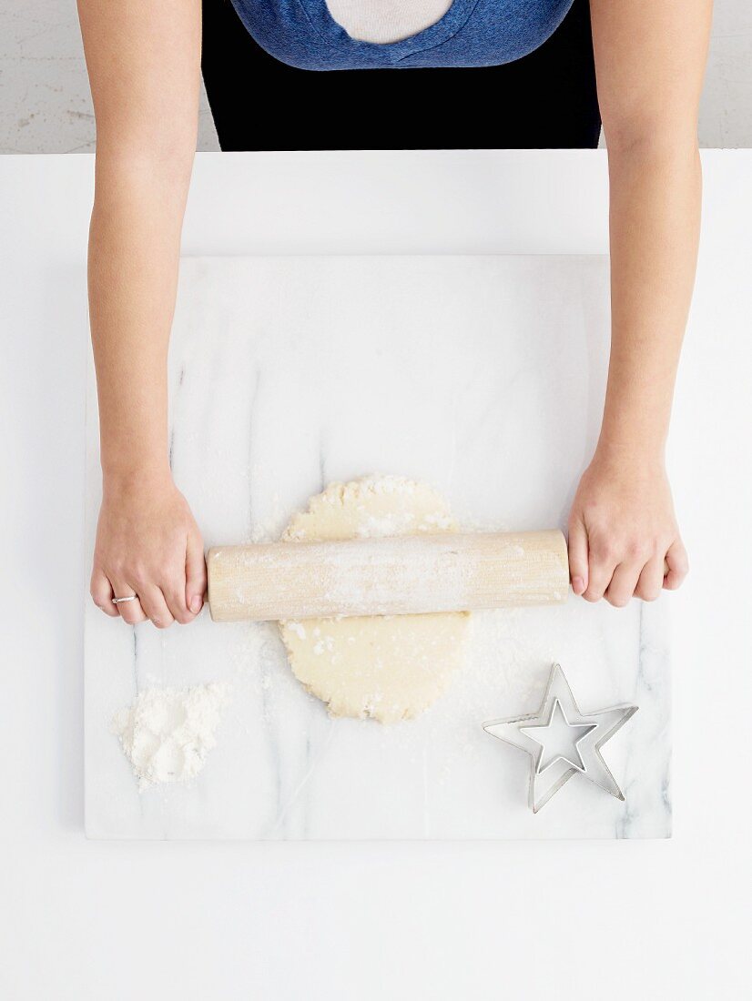 A woman rolling out pastry on a marblew work surface