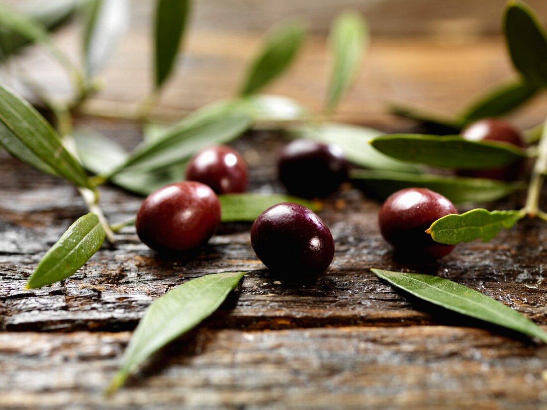 Black olives with leaves on a wooden surface