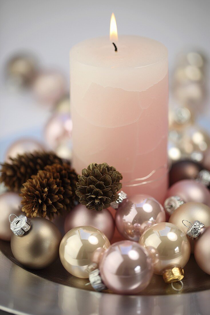 A pink candle with Christmas baubles and pine cones