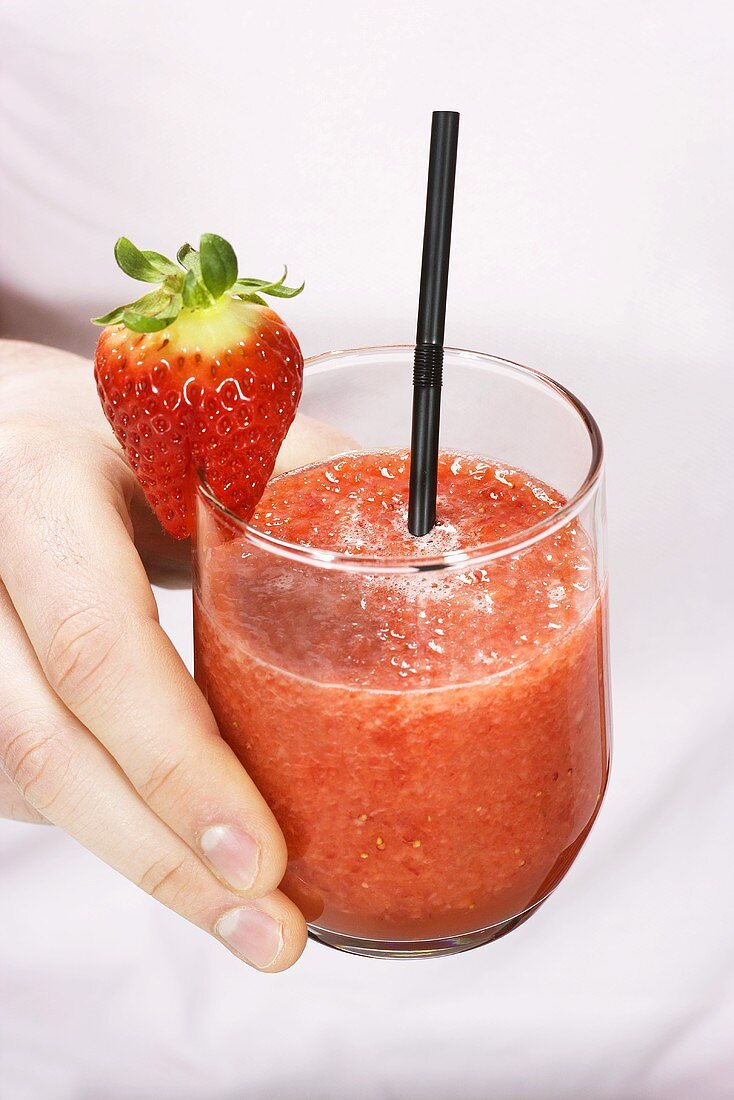 A hand holding a glass of strawberry smoothie