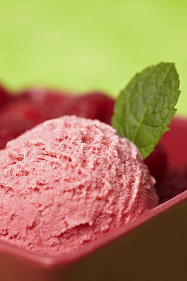 A scoop of raspberry ice cream with a mint leaf and fresh raspberries