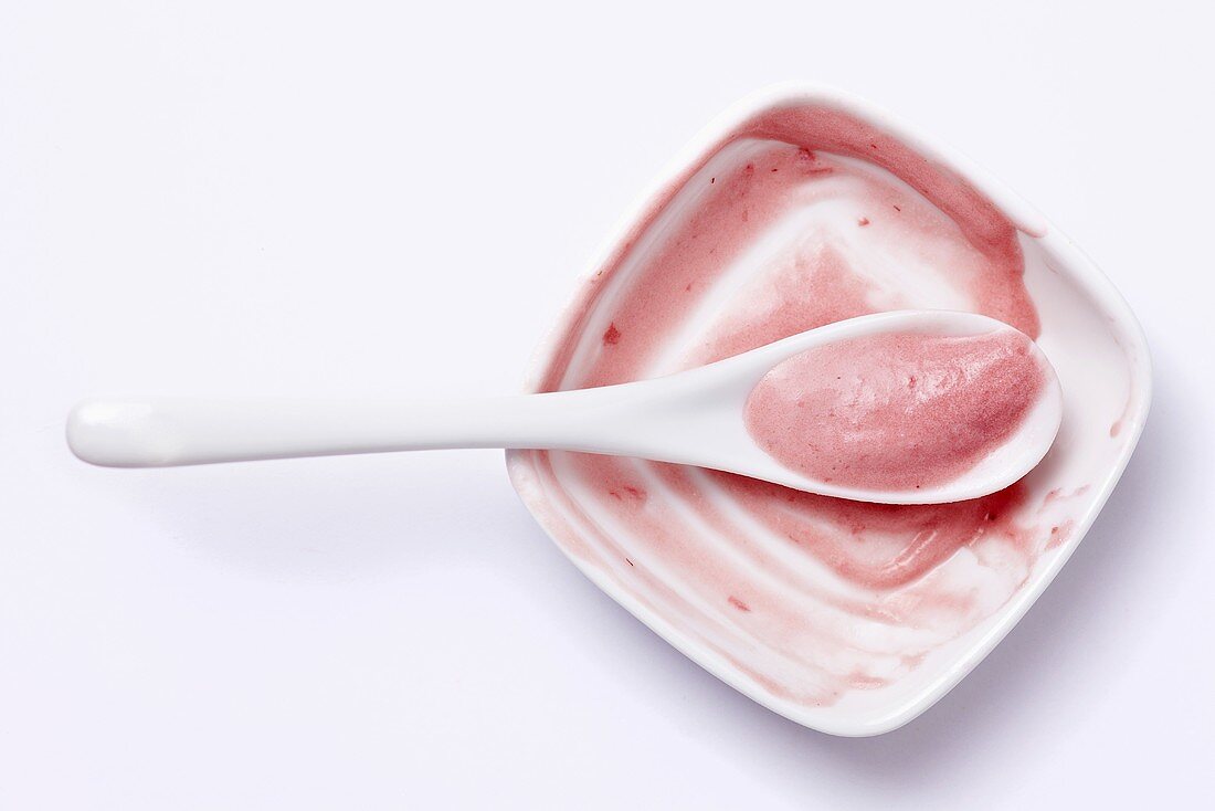 The remains of raspberry ice cream in a bowl with a dirty spoon