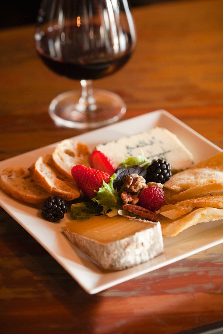 Käseplatte mit Beeren, Nüssen und Brot, Rotweinglas