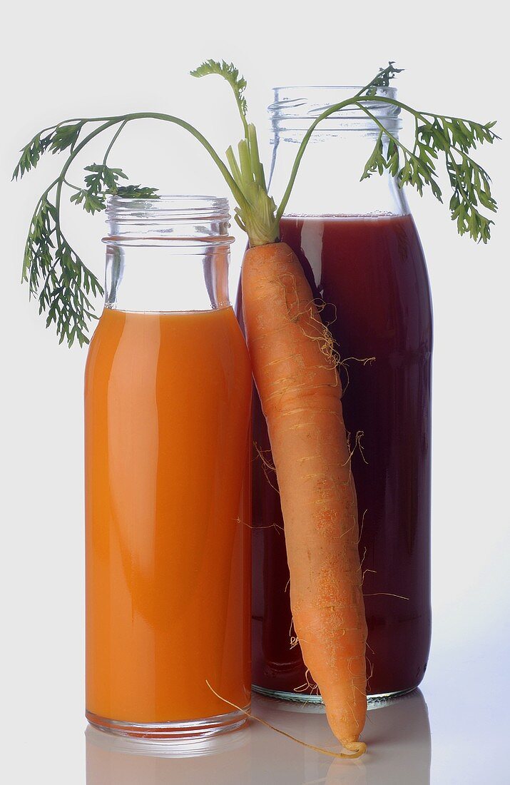 Vegetable juices in bottles and a fresh carrot