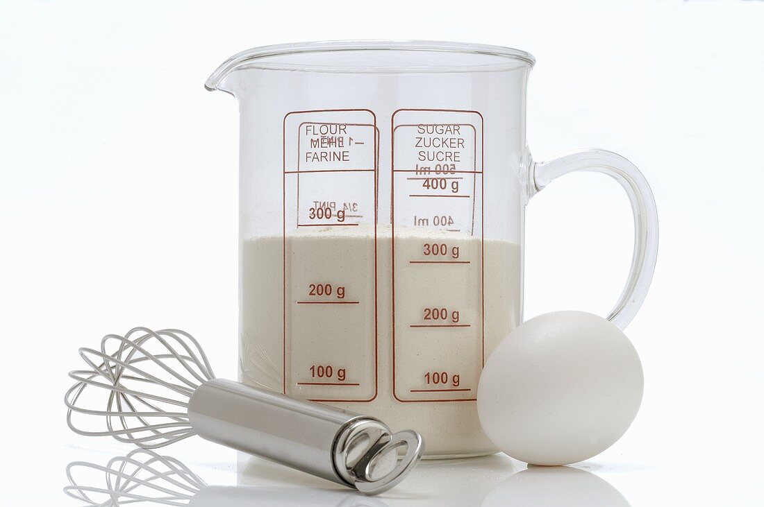 Milk in measuring jug, whisk and egg