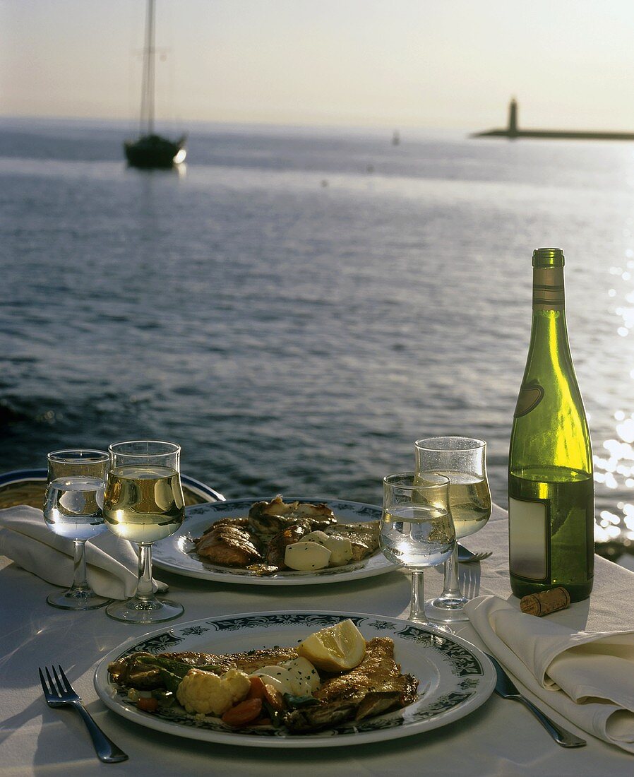 Two plates of food and wine on laid table by sea