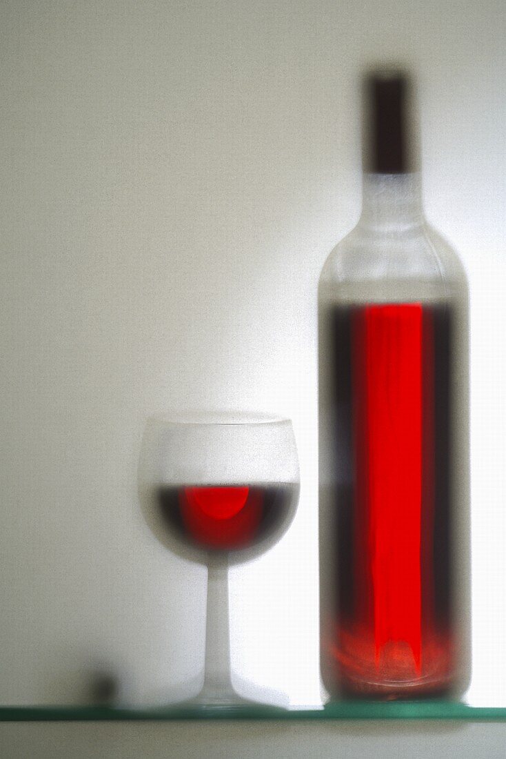 Glass and bottle of red wine (out of focus)