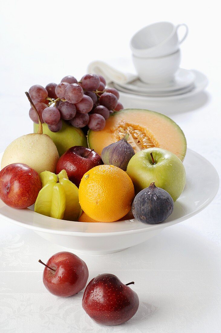 Dish of fruit, white cups and saucers in background