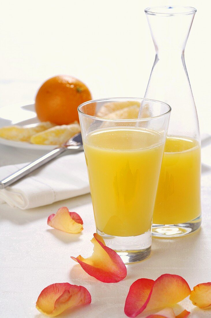 Orangensaft in Glas und Karaffe, Orange im Hintergrund