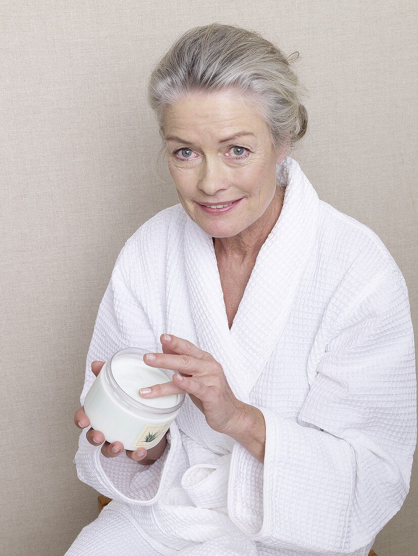 Ältere Frau im Bademantel mit Cremetiegel