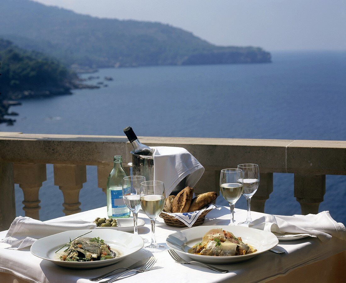 Fish dishes and wine on laid table with sea view