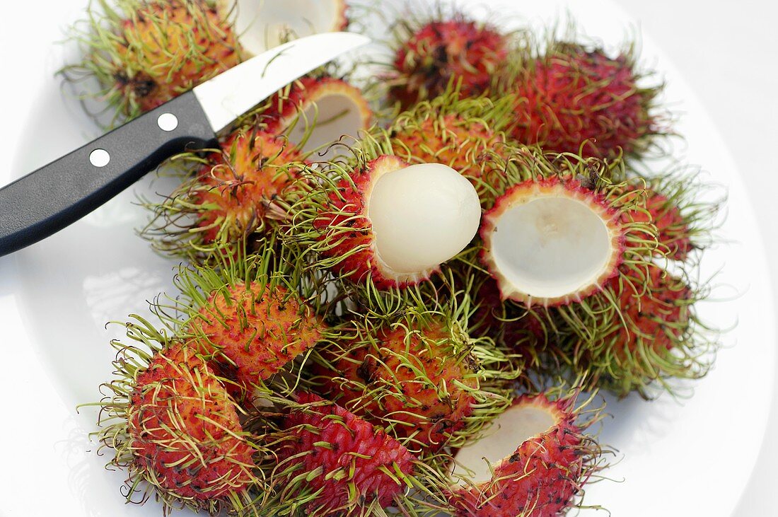 Whole and peeled rambutans on a plate with knife