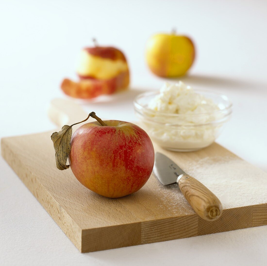 Apfel und ein Schälchen Quark mit einem Messer auf Holzbrett