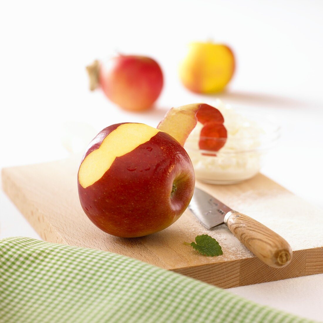 Apfel und ein Schälchen Quark mit einem Messer auf Holzbrett