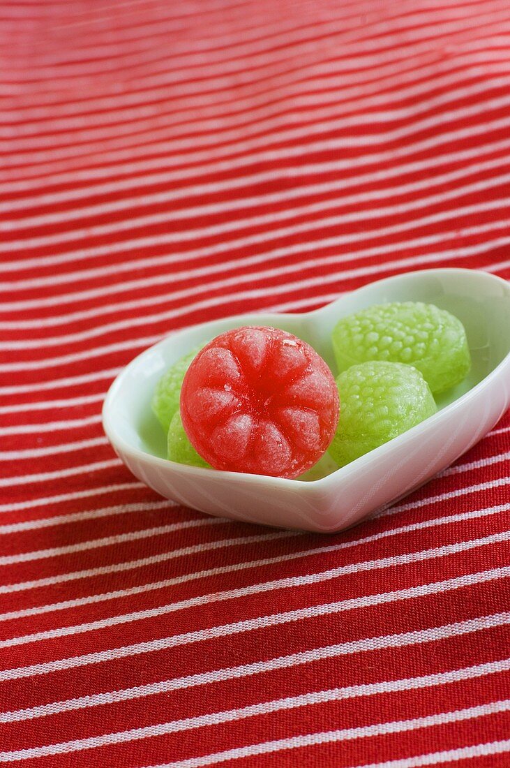 Green sweets and one red sweet in a heart-shaped dish