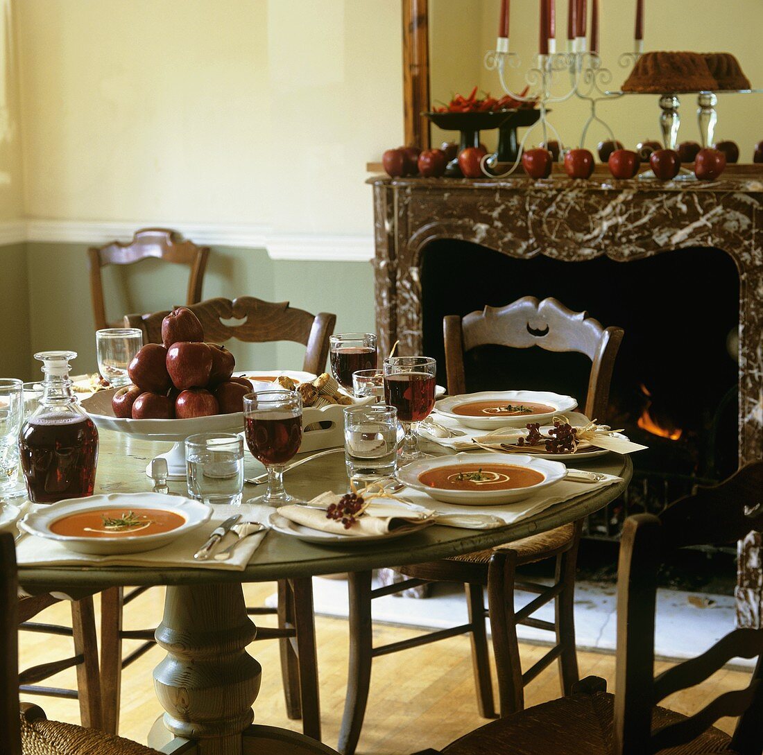 Herbstlich gedeckter Tisch mit Tomatensuppe, Äpfeln, Rotwein