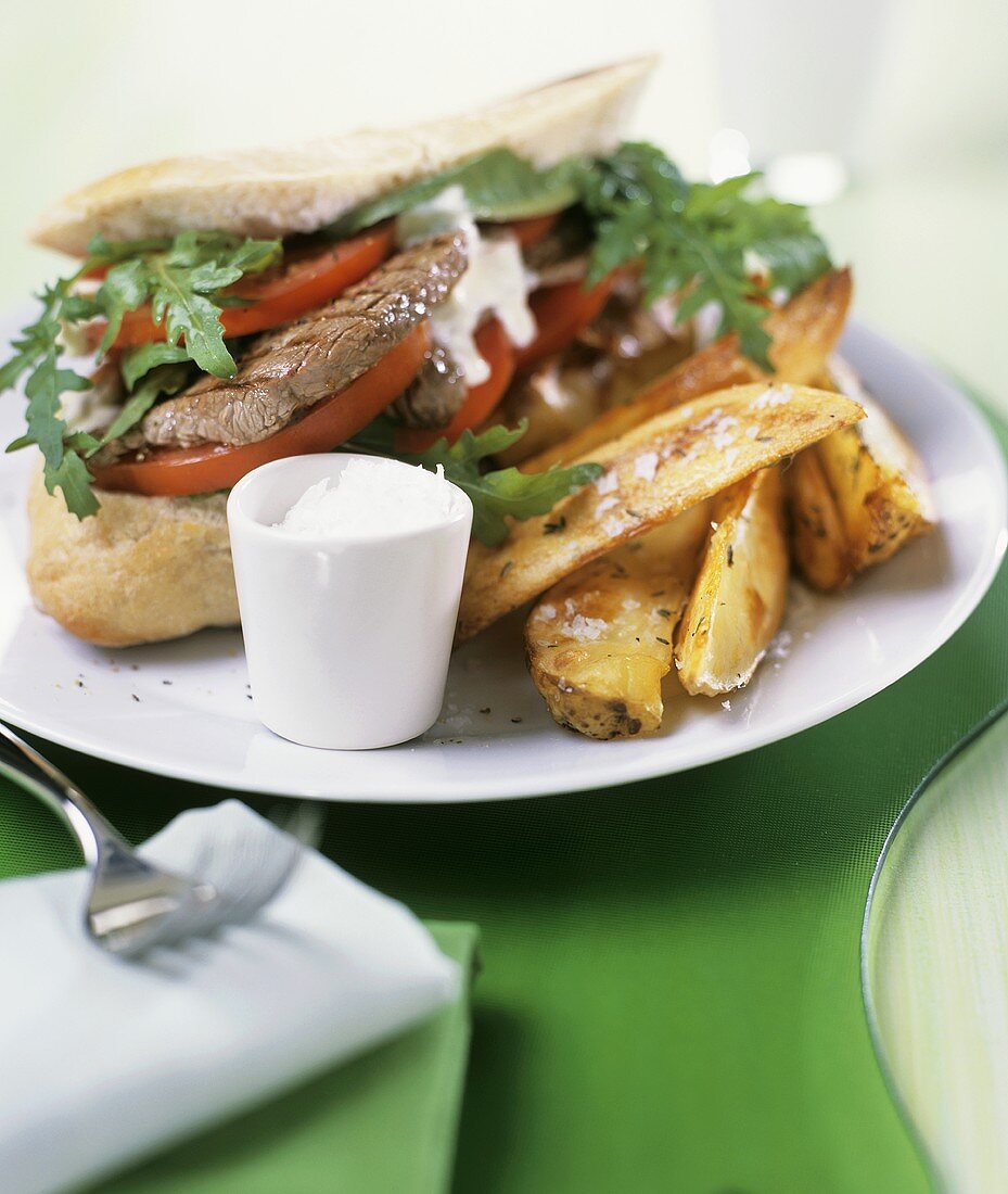 Steak sandwich with rocket, tomatoes and potato wedges