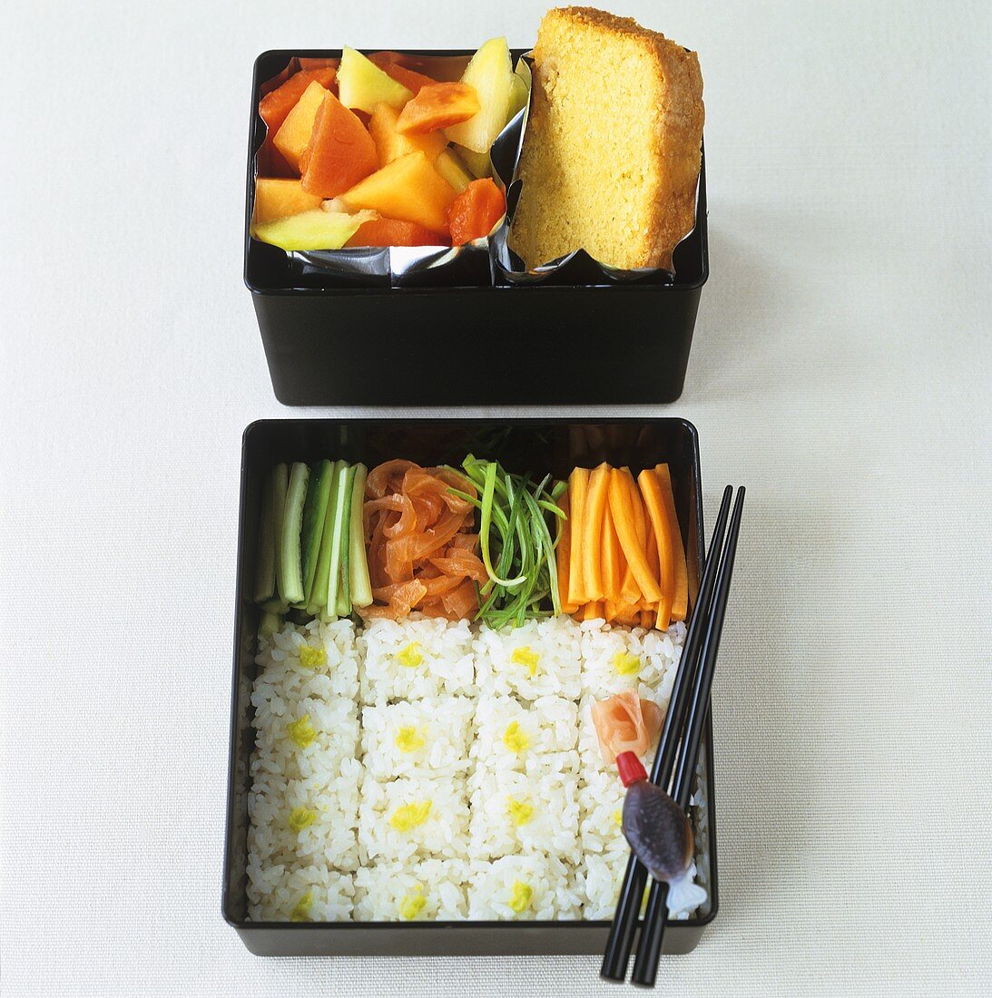 Sushi, vegetables, fruit salad and cake in bento boxes
