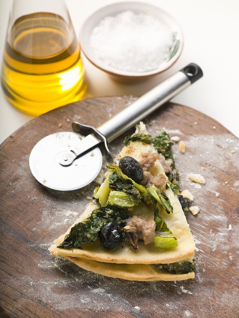 Two pieces of pizza with mince, olives, spinach and cheese