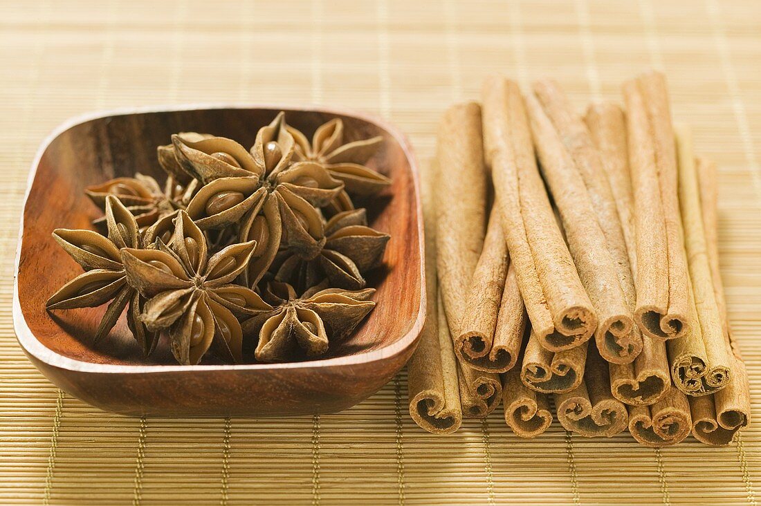 Star anise in wooden bowl, cinnamon sticks beside it