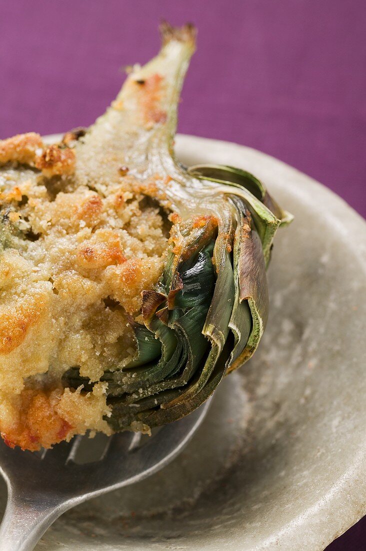 Stuffed artichoke with gratin topping on spoon, close-up