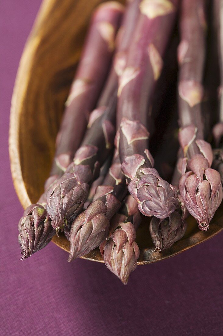 Purple asparagus in wooden bowl