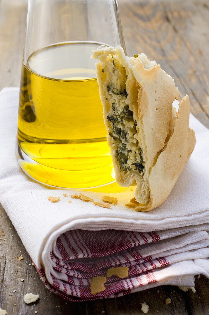 A piece of spinach and ricotta pie beside bottle of olive oil