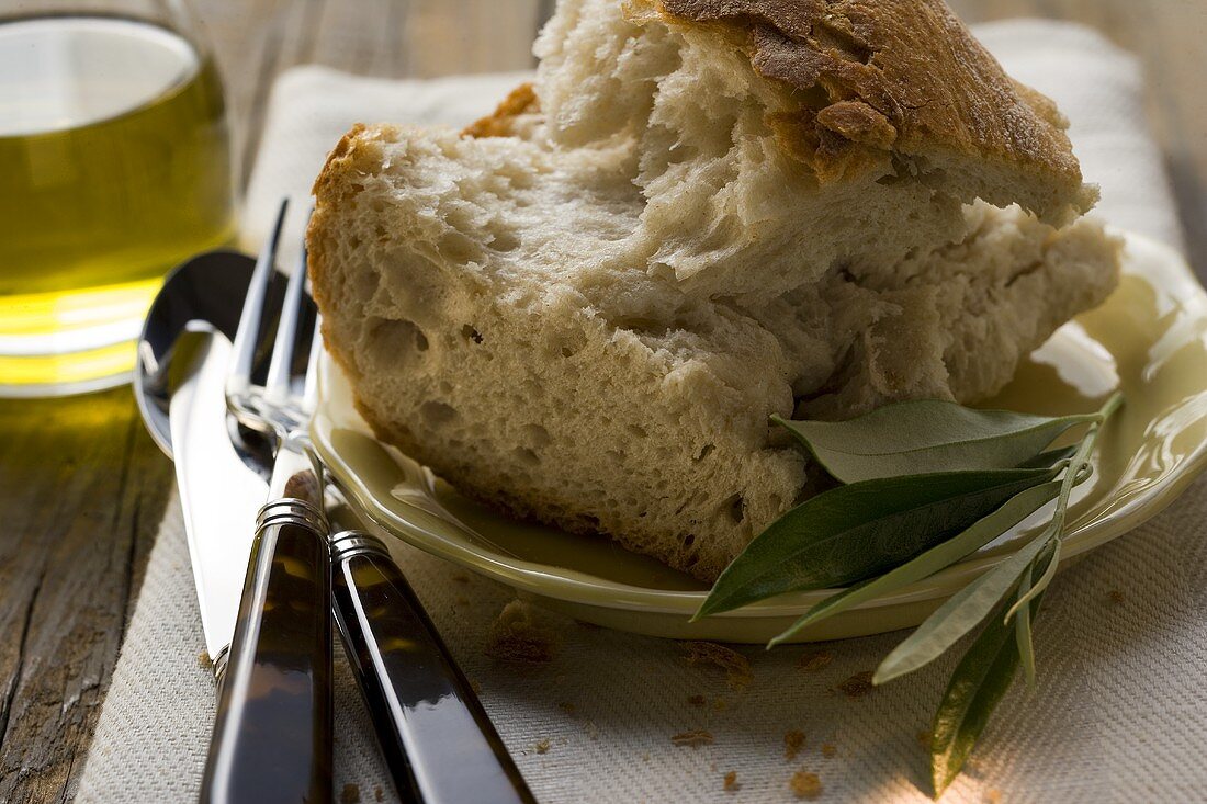 Weissbrotstücke auf Teller mit Olivenzweig, Besteck, Olivenöl