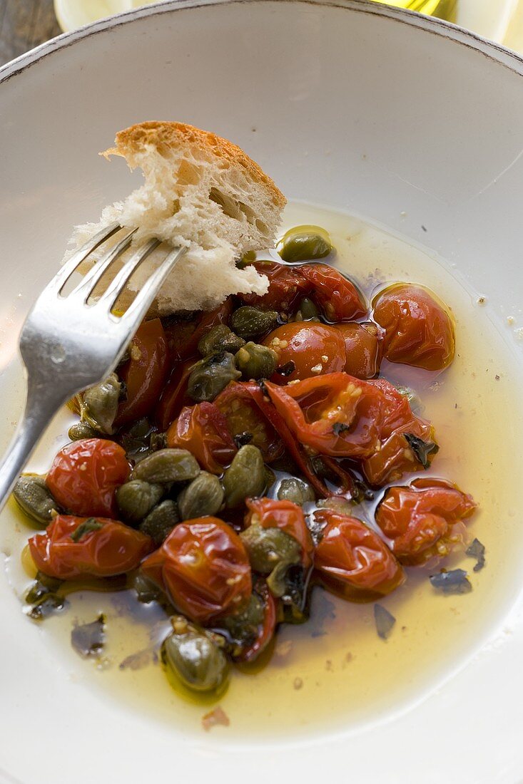 Roasted tomatoes with capers, white bread on fork