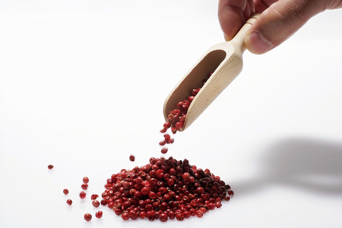 Hand dropping red peppercorns from wooden scoop
