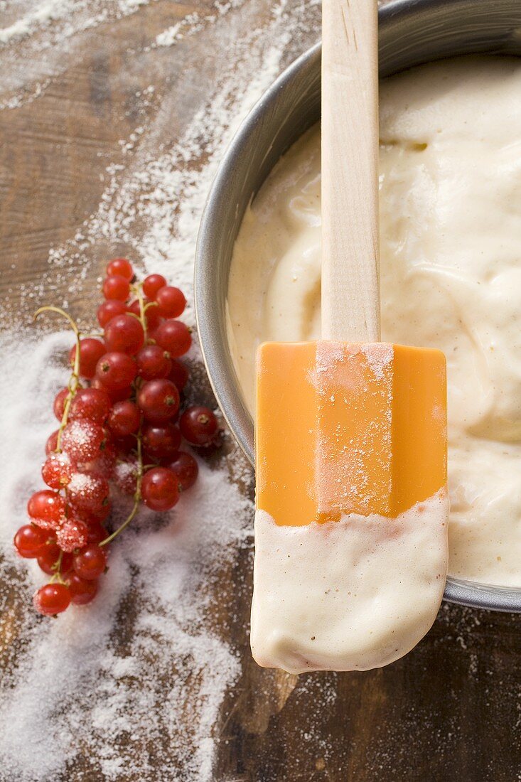 Cake mixture in baking tin with spatula, redcurrants, sugar