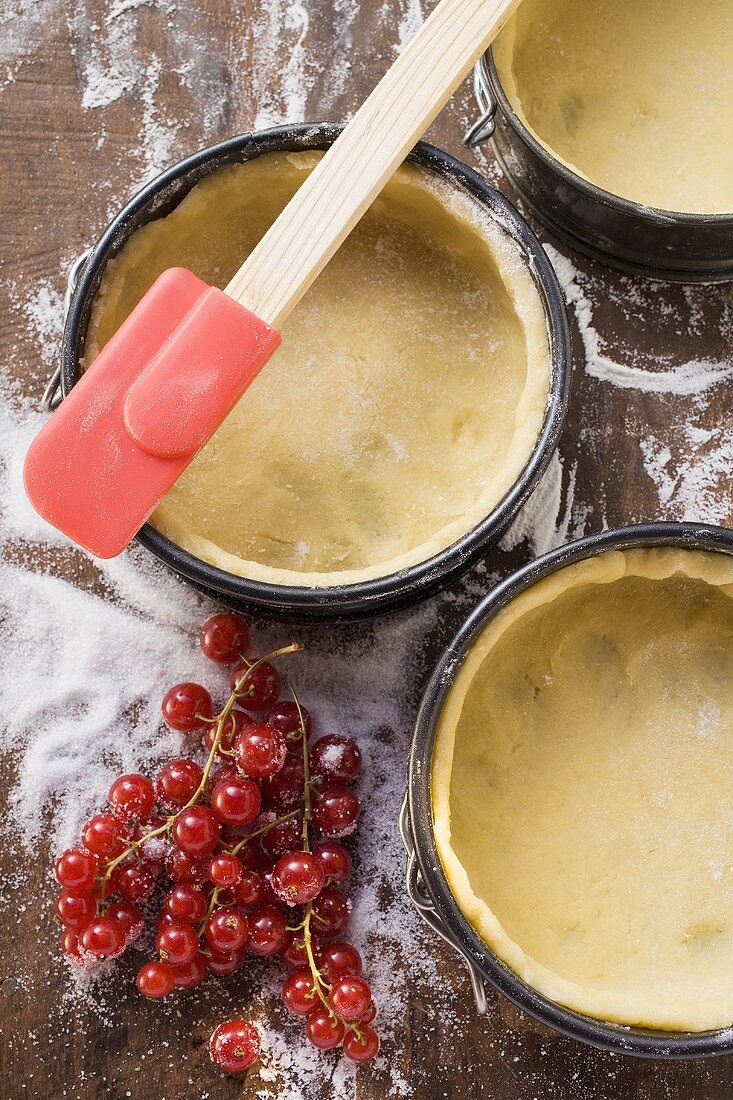 Baking tins lined with pastry, spatula, redcurrants