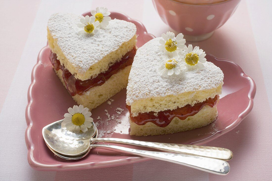 Herzförmiges Gebäck mit Marmelade, Puderzucker, Gänseblümchen